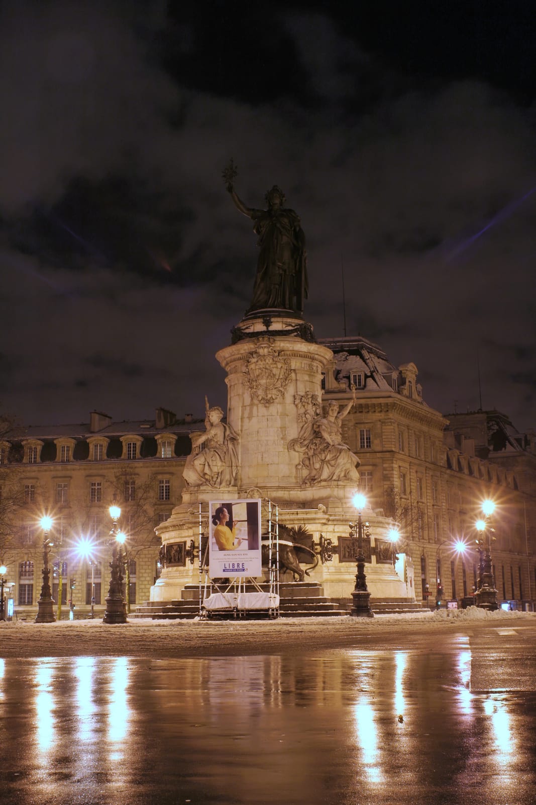 Portrait or photograph of Aung San: Monument au milieu de la place de la République, de nuit sous la neige, avec affiche appelant à la libération de Aung San Su