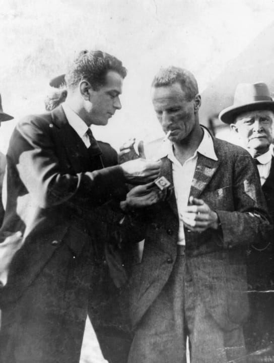 Portrait or photograph of Charles Kingsford Smith: Sir Charles Kingsford Smith An associate offers the aviator Kingsford Smith a light for his cigarette. Sir Ch