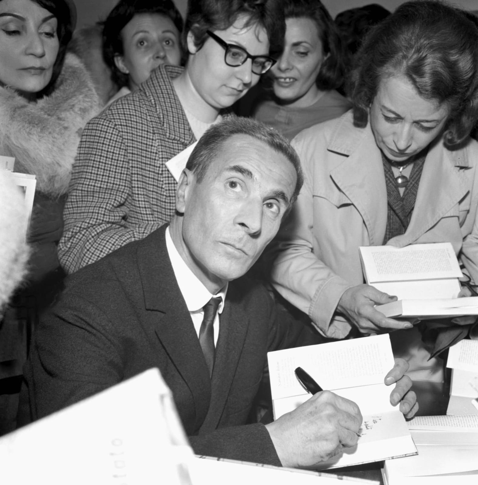 Portrait or photograph of Dino Buzzati: Photograph of the Italian writer Dino Buzzati signing his books in a Milan bookstore.