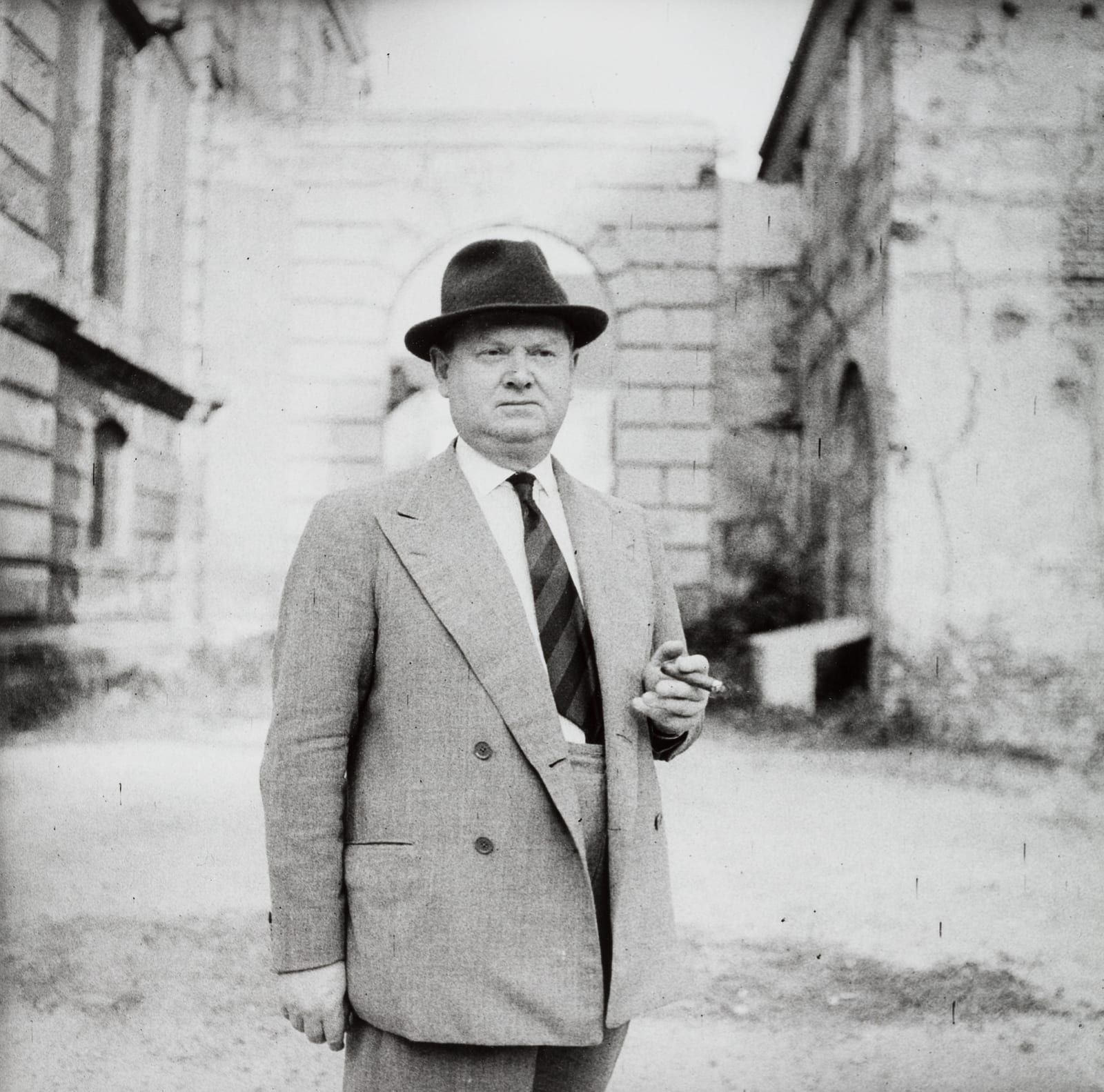 Portrait or photograph of Evelyn Waugh: Evelyn Waugh, Hüftporträt mit Zigarre, zum rechten Bildrand gedreht, vor Ruine, 1959, Gelatineentwicklungspapier (Baryt)