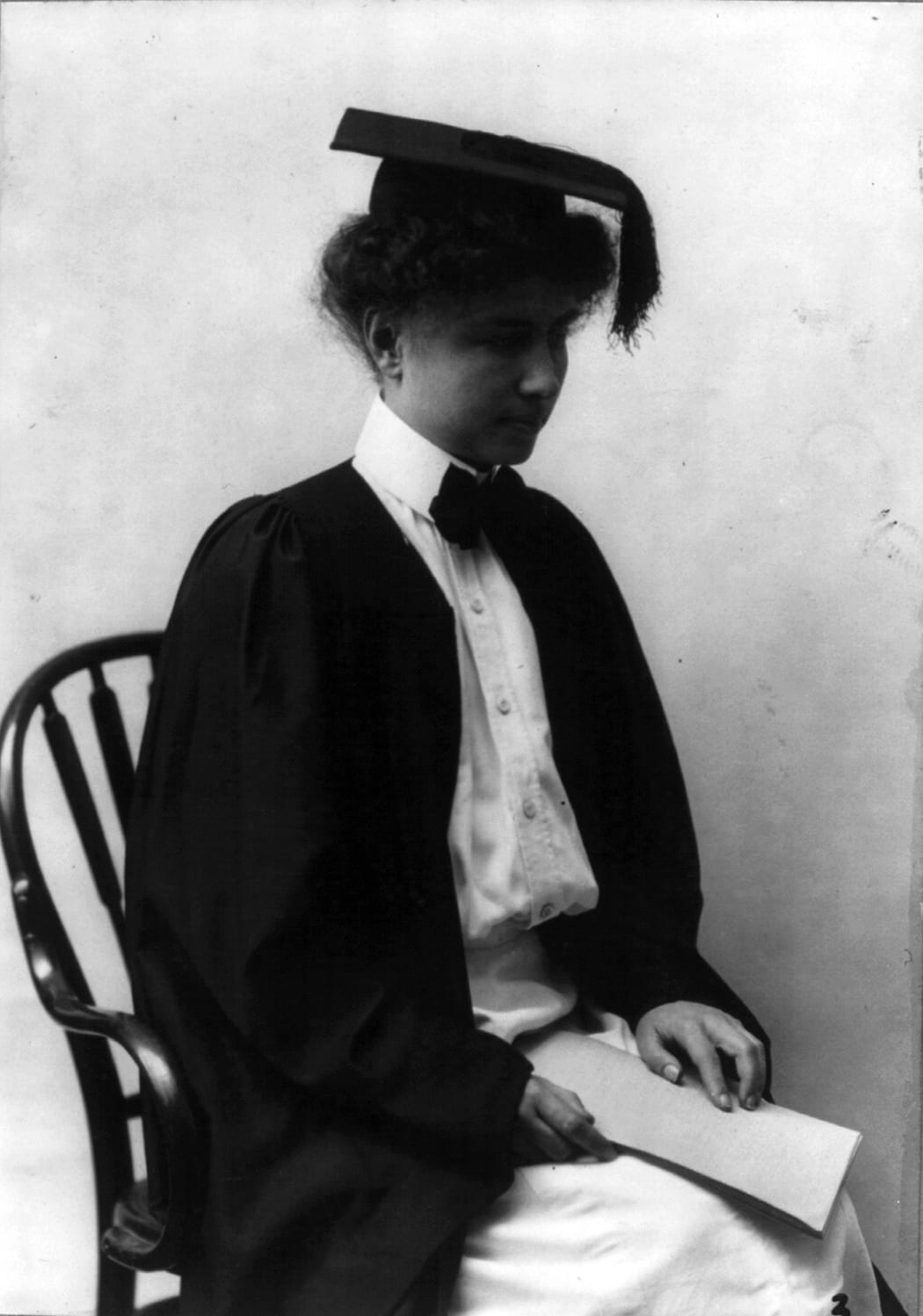 Portrait or photograph of Helen Keller: Helen Keller : Portrait, 3/4 length, seated, facing right, wearing academic robe and cap.