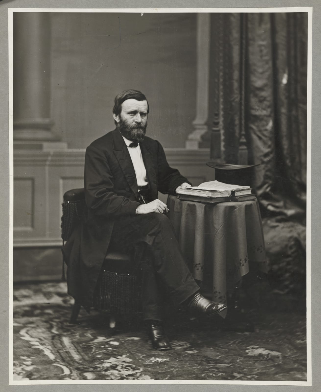Portrait or photograph of Ulysses S. Grant: Ulysses S. Grant, full-length portrait, seated at table with books and top hat, facing right